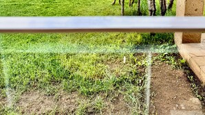 A view through a window of a giraffe enclosure with a grassy field, trees, and a building in the background. - Lookout sirwa
 (Naivasha)
