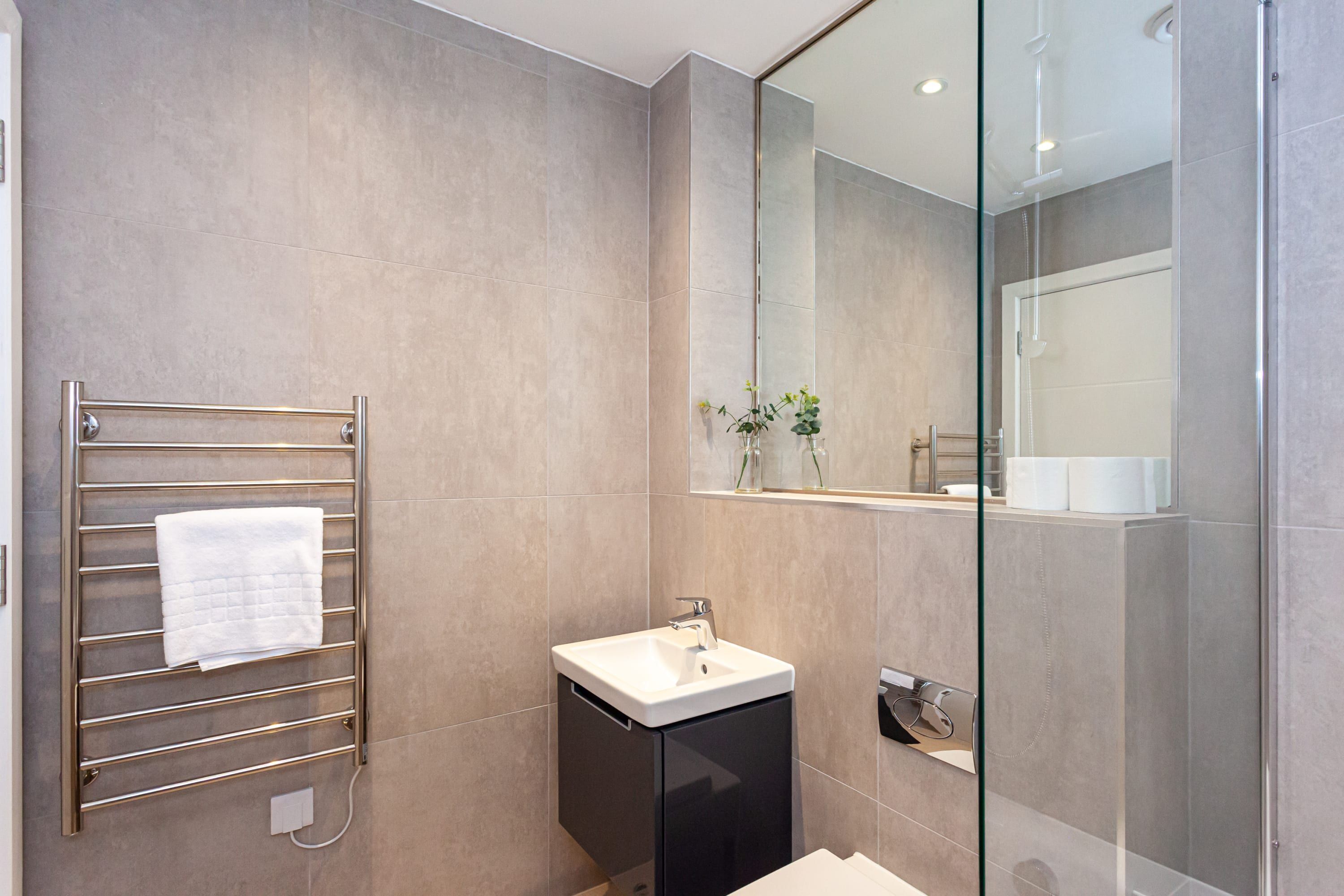 A modern bathroom with a glass shower enclosure, a black cabinet with a white sink, and a towel rack with a white towel.