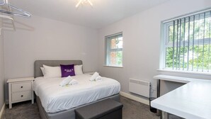 A bedroom with a bed, bedside tables, a bench, a window, and a desk. - Lovely One-bedroom Serviced Apartment in Eccles (Manchester)