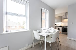 Une cuisine moderne avec des armoires blanches, un four encastré et un coin repas comprenant une table et des chaises blanches.