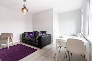Un salon moderne avec un canapé en cuir noir, une chaise en bois, une table à manger avec des chaises et un tapis violet.