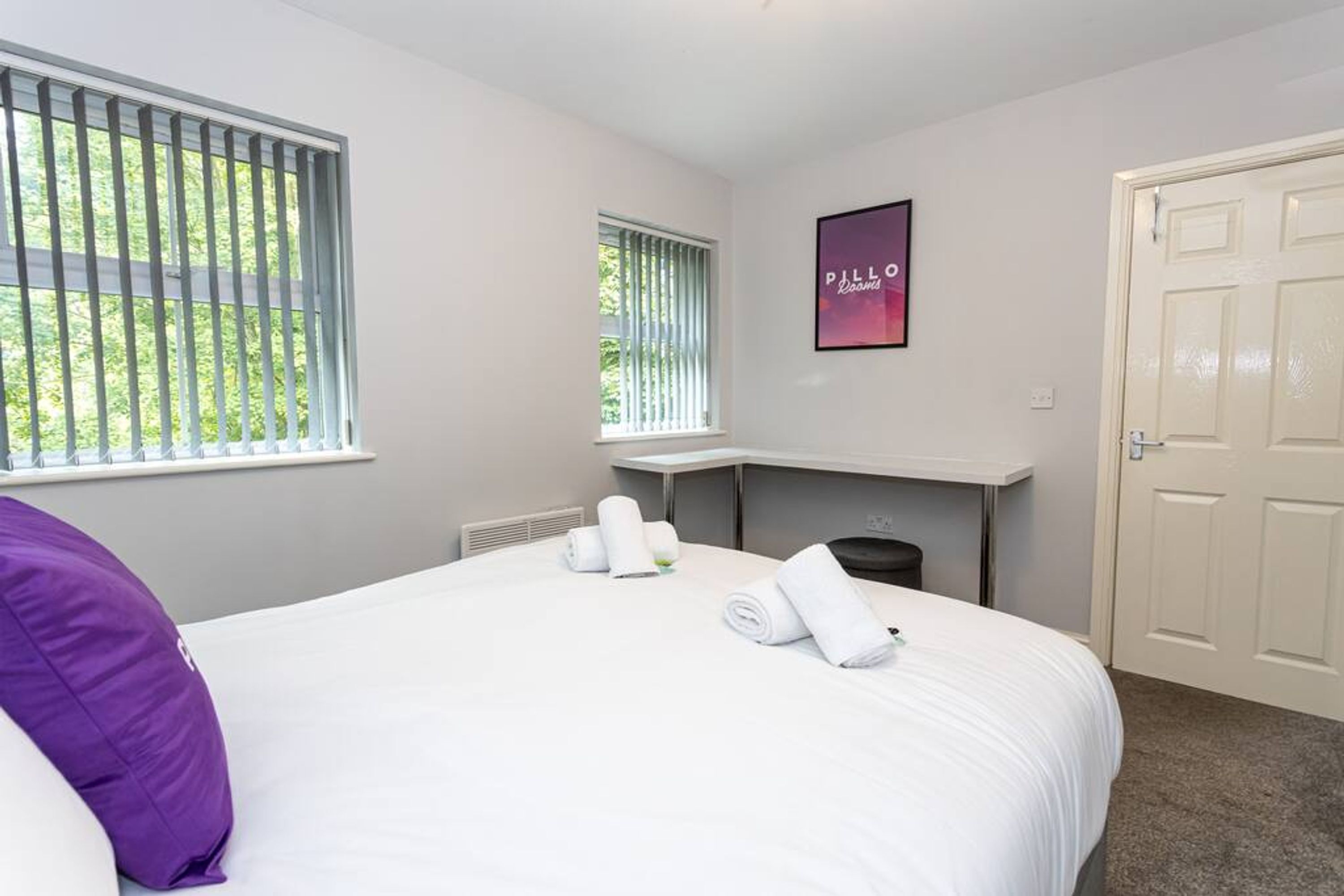 A hotel room with a large bed, a fireplace, a window with blinds, and a door.