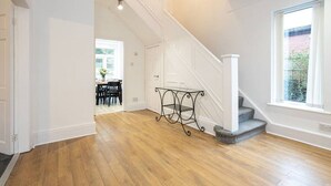 A spacious hallway with wooden flooring, a staircase with white railings, and a large window providing natural light.