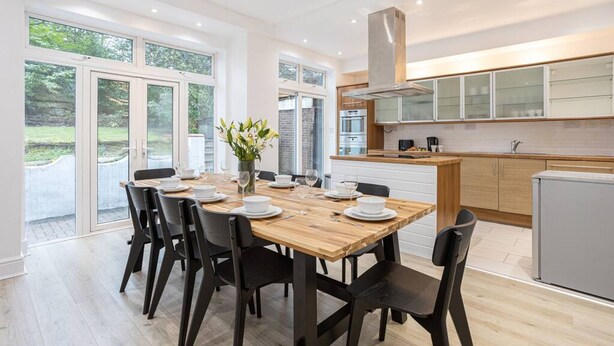 A modern kitchen with a wooden table set for dining, a built-in oven, and a stainless steel range hood.