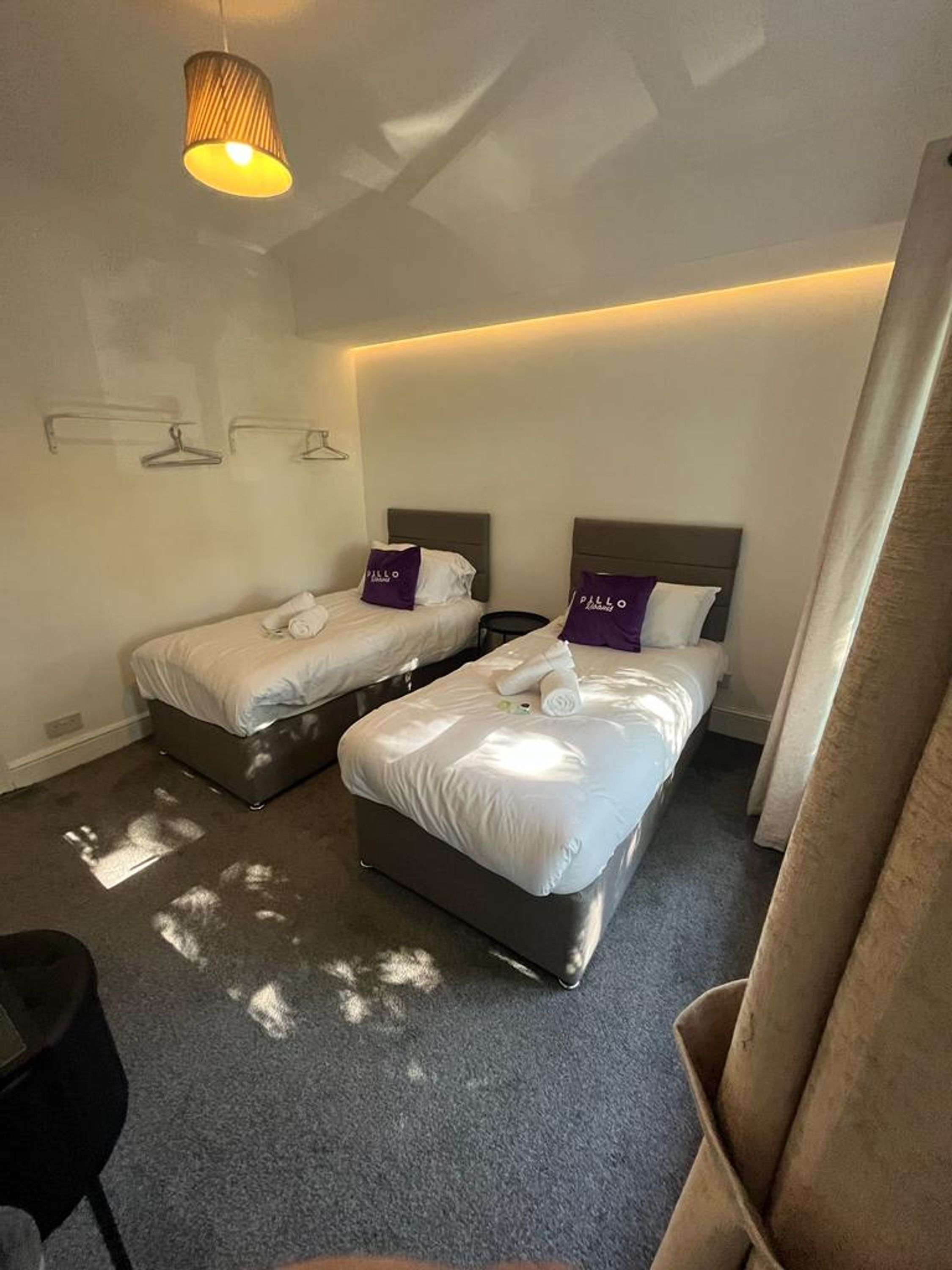 Een hotelkamer met twee bedden, een hanglamp en een klein tafeltje.