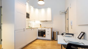 Una cocina moderna con armarios blancos, horno empotrado y comedor con una mesa para dos.