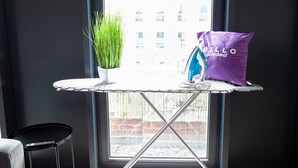 Ein Fenster mit Blick auf Gebäude, ein kleiner Tisch mit Pflanze und einem violetten Kissen, sowie ein Stuhl.