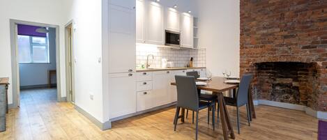 A modern kitchen with white cabinets, a brick fireplace, and a dining area with a wooden table and chairs.