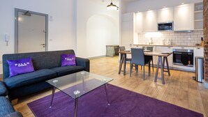 A modern living room with a glass coffee table, a sofa with purple cushions, and a dining area with a table and chairs. - Apartment Close to City Centre and Media City By Pillo Rooms (Salford)