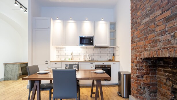 A modern kitchen with white cabinets, a brick fireplace, and a dining area with a wooden table and chairs. - Apartment Close to City Centre and Media City By Pillo Rooms (Salford)