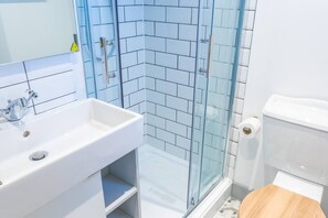 Kylpyhuone, jossa on valkoinen pesuallas, lasinen suihkuseinä ja wc.
