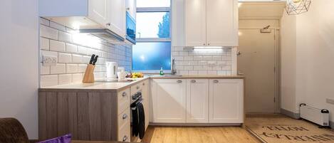 Cocina compacta con armarios blancos, encimera de madera y una ventana que proporciona luz natural.