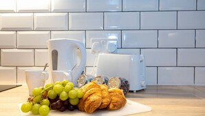 A kitchen counter with a cutting board, a toaster, a coffee maker, a cup, and a plate with grapes and croissants. - Unique 1 Bedroom Apartment by Pillo Rooms (Salford)