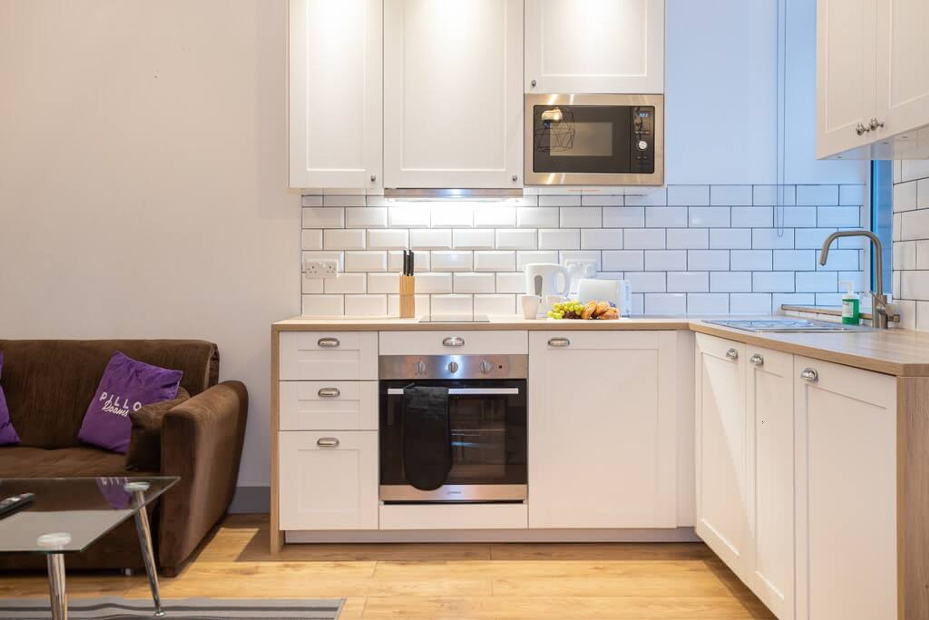 A modern kitchen with white cabinets, a built-in oven, a microwave, and a sink.