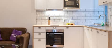 A modern kitchen with white cabinets, a built-in oven, a microwave, and a sink.