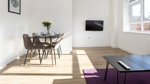 A modern living room with a dining area, a flat-screen TV mounted on the wall, and a large window providing natural light. - Modern, Stylish 1BR Apartment Nearby AO Arena (Manchester)