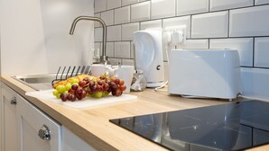 Una cocina moderna con un lavamanos de acero inoxidable, una tabla de cortar con uvas y pan, una cafetera y un tostador.