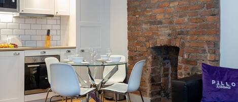 A modern kitchen with white cabinets, a brick wall, and a dining area with a glass table and white chairs.