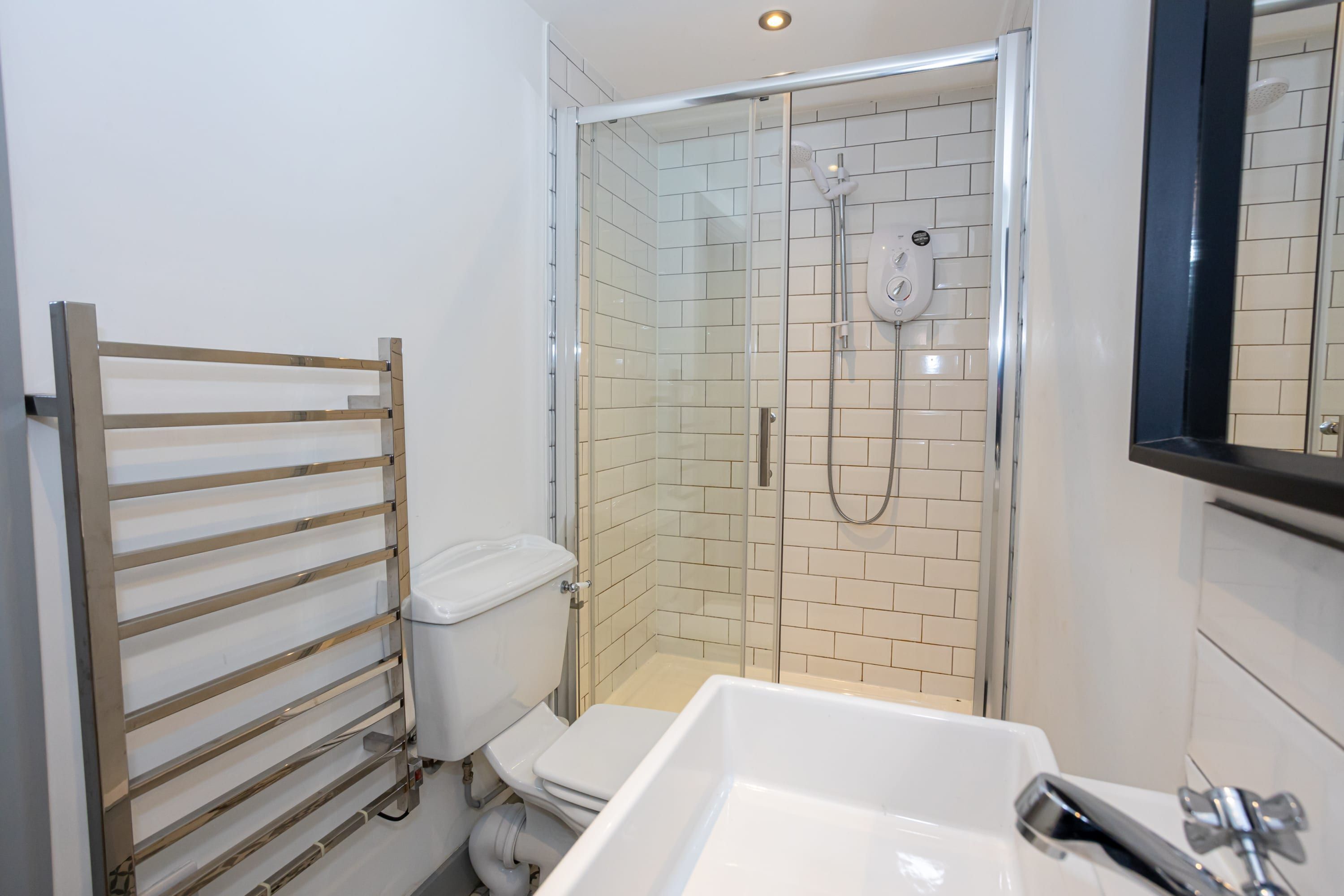 Ein modernes Badezimmer mit einer gläsernen Duschkabine, einem weißen Waschbecken und einem Handtuchhalter.