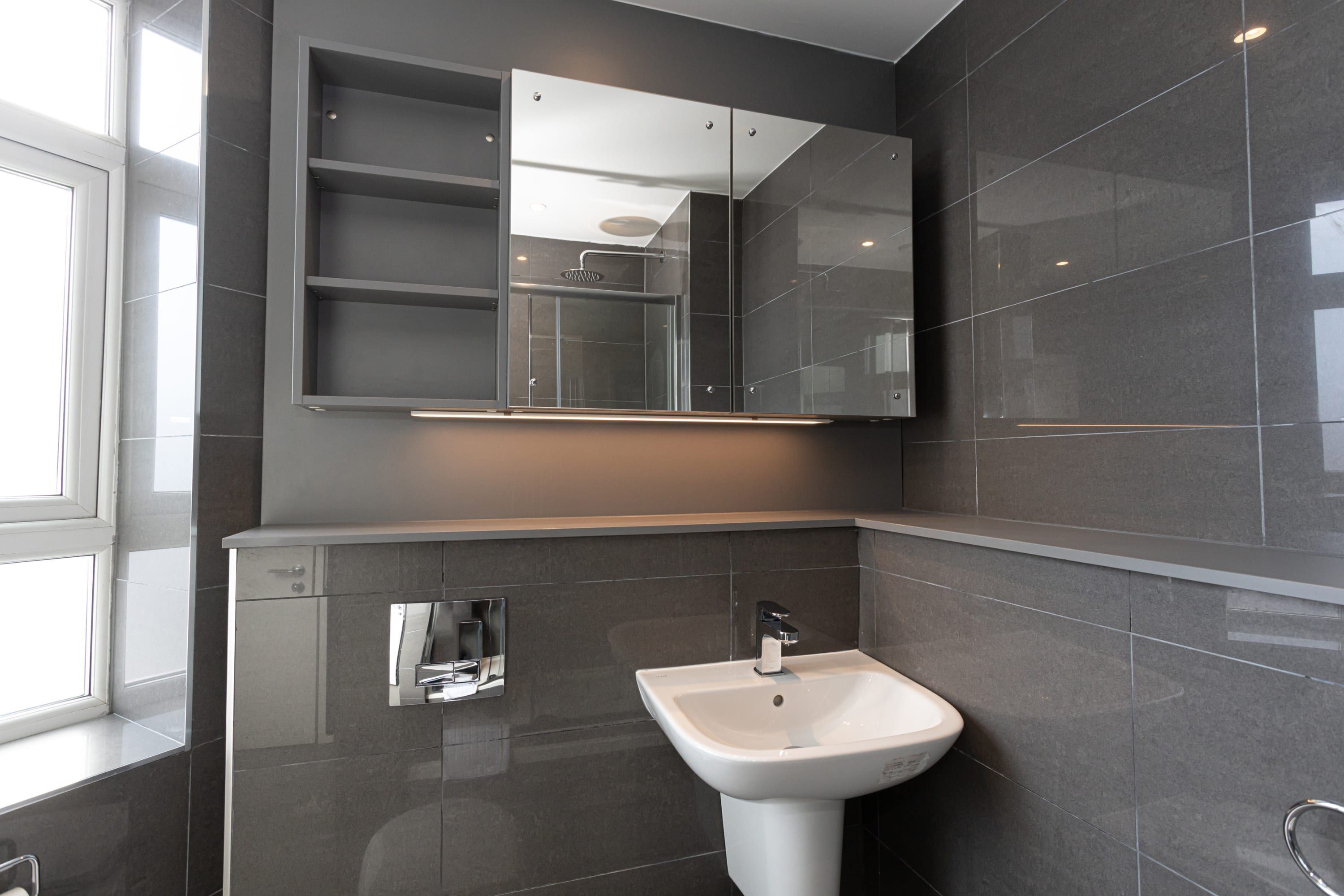Un baño moderno con un lavamanos pedestal blanco, un espejo grande y una cabina de ducha con paredes de vidrio.