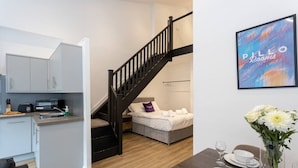 A compact living space with a kitchenette, a bed with a purple pillow, a dining area with a table set for two, and a staircase. - Modern and Spacious Duplex in Manchester City Centre (Manchester)