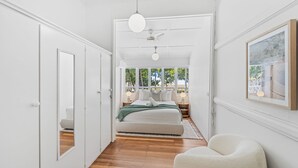 Un dormitorio con cama, mesita de noche, silla y un amplio ventanal con vistas a árboles.