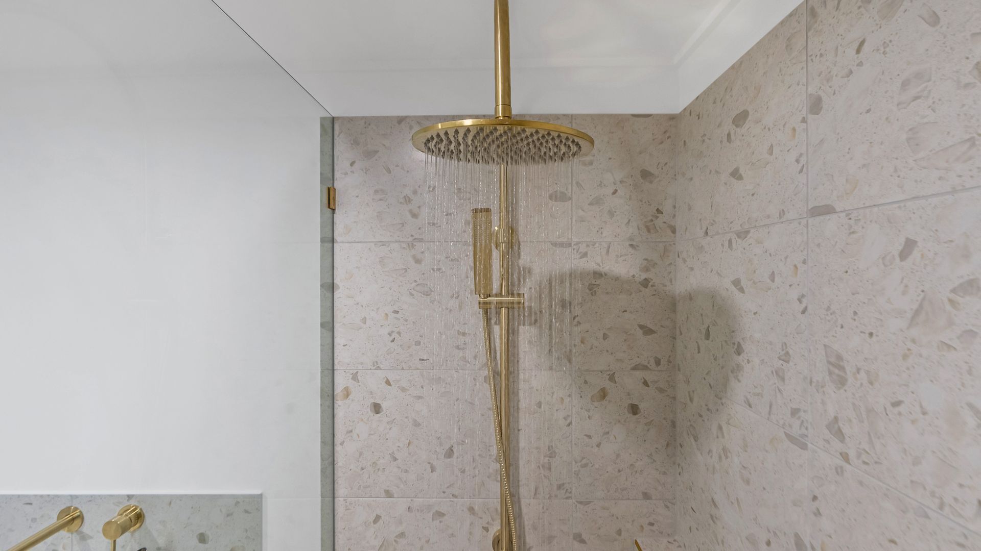 A modern shower with a gold showerhead and a vertical rain shower head.