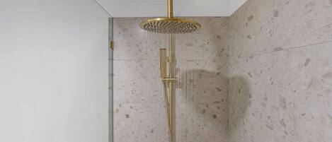 A modern shower with a gold showerhead and a vertical rain shower head.