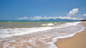 Una playa con olas, cielos despejados y montañas a lo lejos.