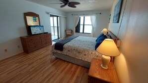 Ein Schlafzimmer mit Bett, Kommode, Deckenventilator und einem Fenster mit Vorhängen.