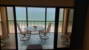 Ein Balkon mit Glastisch und Stühlen mit Blick auf einen Strand.