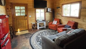 A cozy cabin interior with a wooden interior, a fireplace, a television, and a red chair. - Lava Hot Springs Country Cabin (Bancroft)