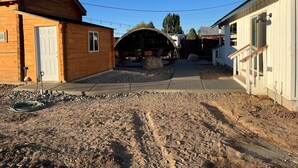 A wooden cabin with a covered outdoor seating area, a concrete pathway, and a gravel driveway. - Lava Hot Springs Country Cabin (Bancroft)