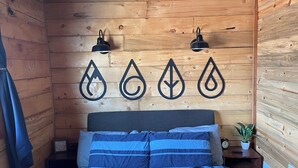 A wooden cabin bedroom with a bed, two wall-mounted lamps, and a wall decoration of water droplet symbols. - Lava Hot Springs Country Cabin (Bancroft)
