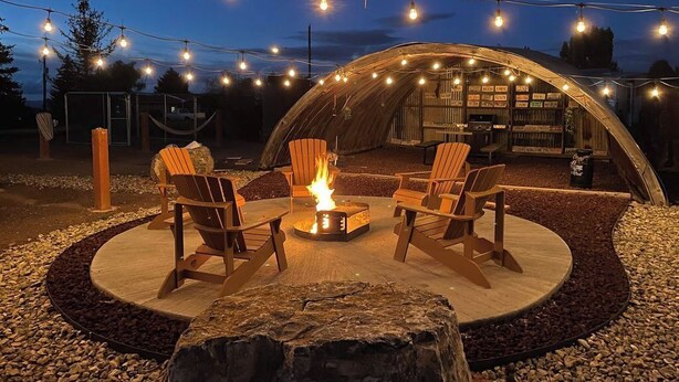 An outdoor seating area with wooden chairs and a central fire pit, surrounded by a circular stone path and string lights. - Lava Hot Springs Country Cabin (Bancroft)