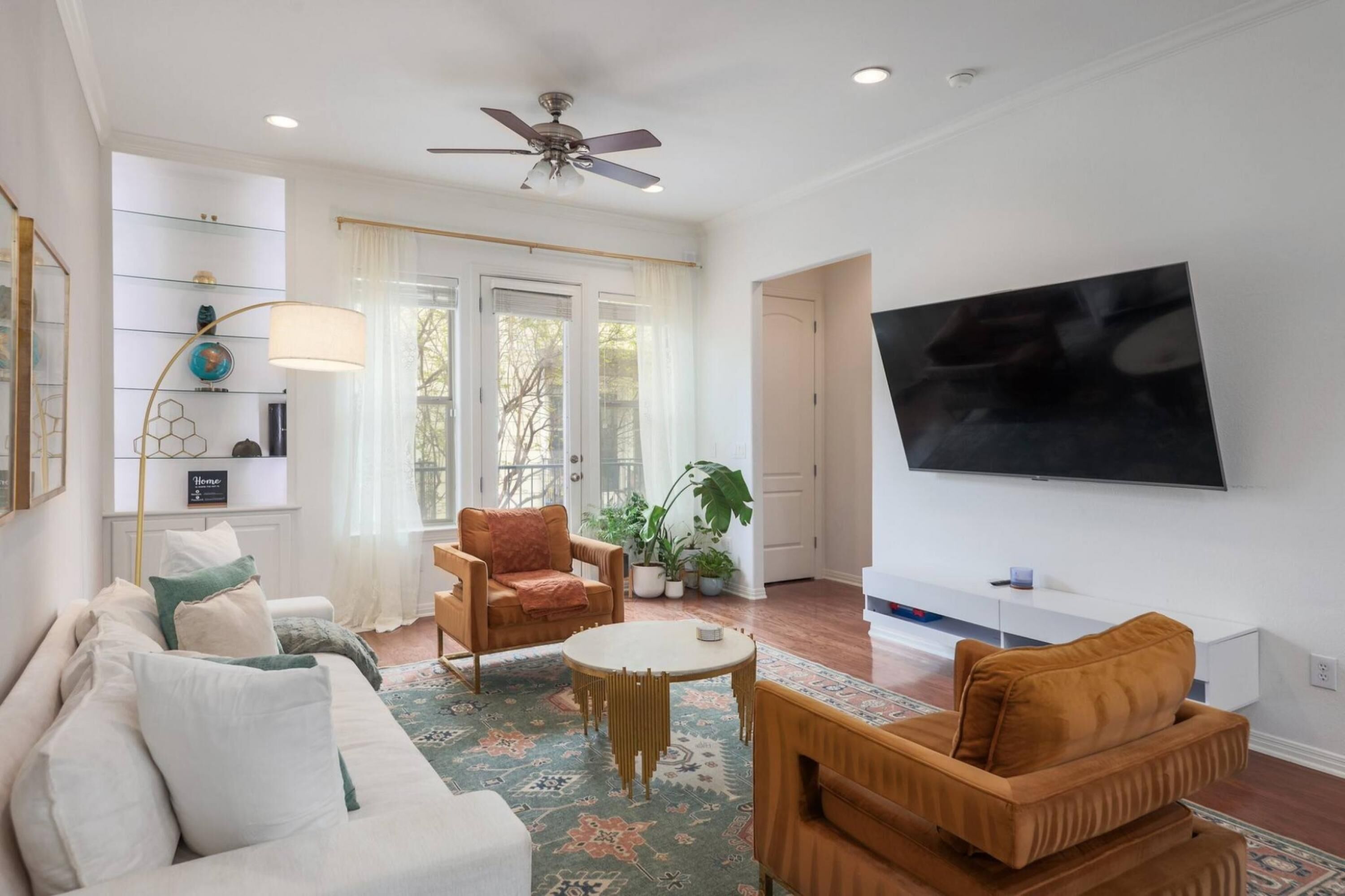 A living room with a sofa, armchairs, a coffee table, a TV, and a ceiling fan.