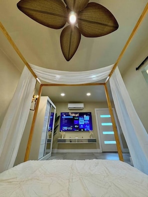 Un dormitorio con ventilador de techo, cama, televisión y baño.
