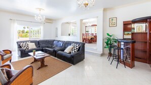 Amplia sala de estar con sofá seccional, una mesa de centro y una zona de bar con taburetes.