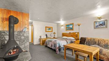 A cozy room with a stone fireplace, a bed with a wooden headboard, a wooden table, and a sofa.
