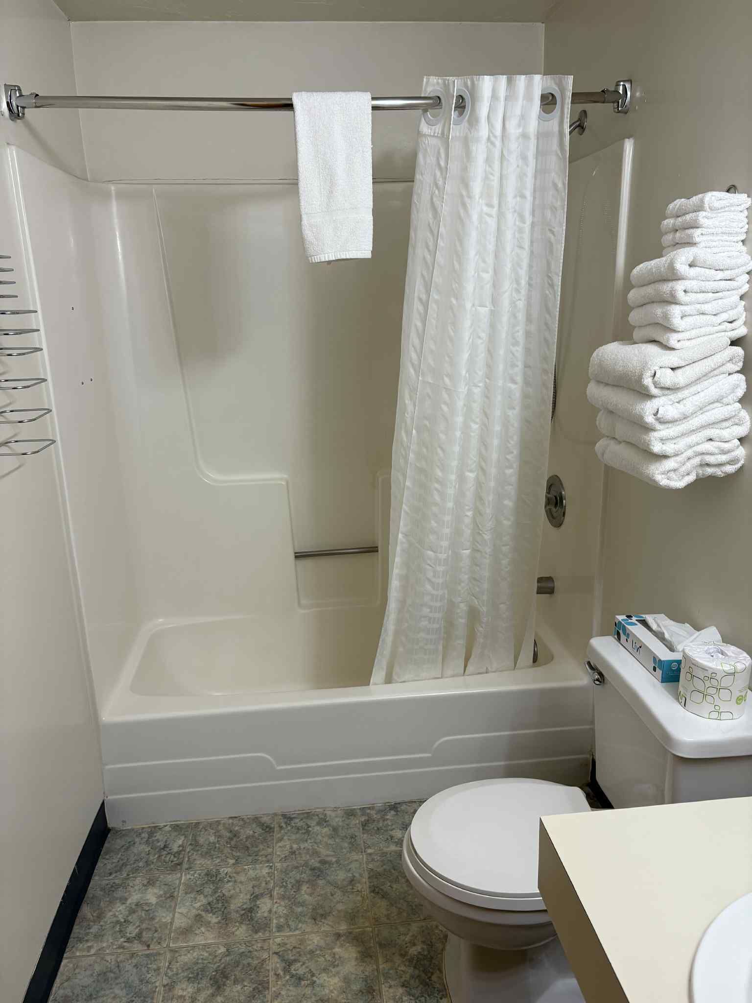 Un baño con bañera, inodoro y toallero con toallas dobladas.