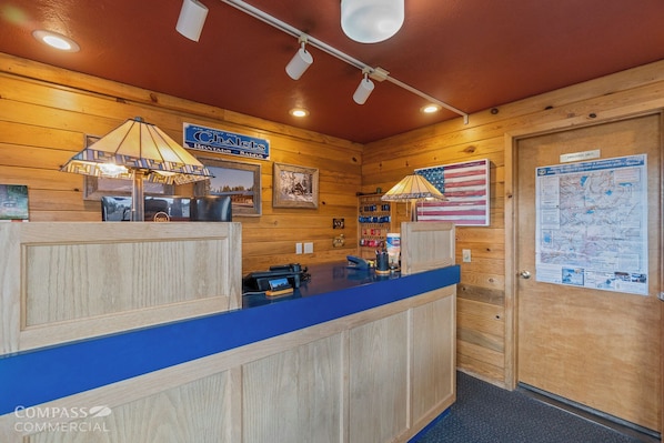 A reception desk with a blue counter, wooden paneling, and a map on the wall. - Willamette Pass Inn (Crescent)