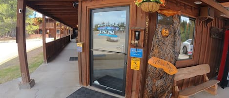 A wooden building entrance with a glass door, a wooden bench, and a welcome sign.