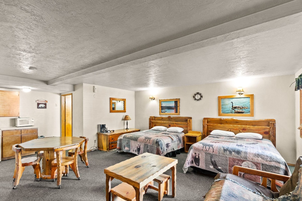 Une chambre avec deux lits, une table en bois, un bureau et une chaise. On y trouve également un four à micro-ondes et un placard.