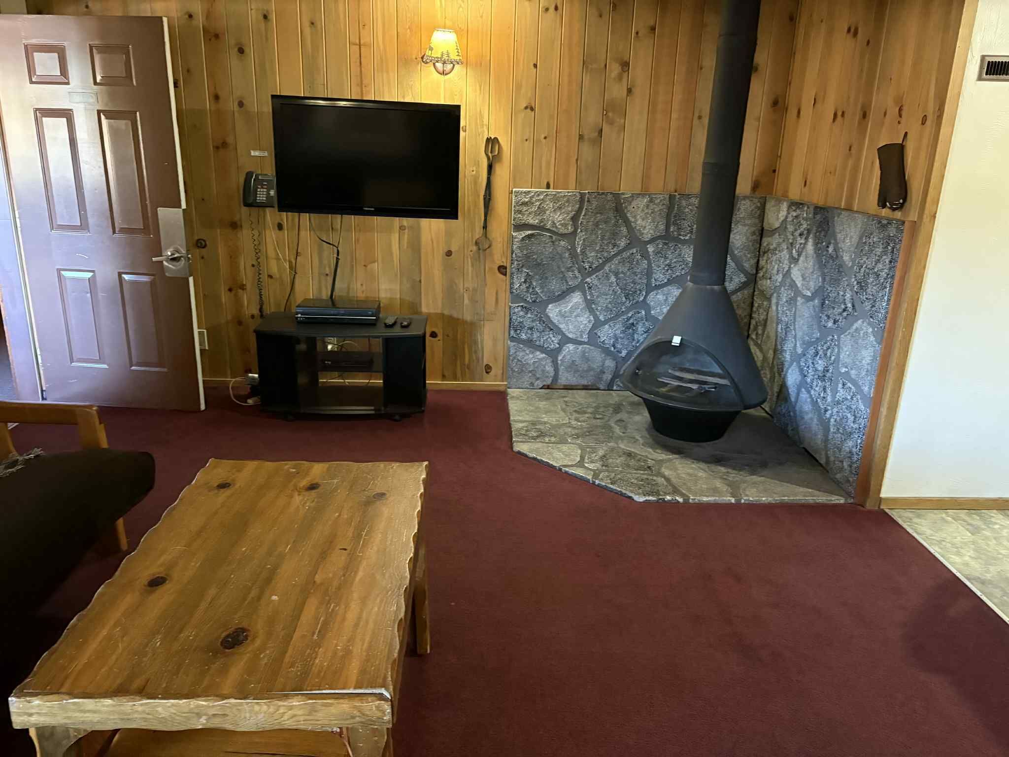 Una habitación acogedora con chimenea de piedra, televisión en la pared y una mesa de madera.
