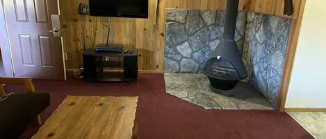 Una habitación acogedora con chimenea de piedra, televisión en la pared y una mesa de madera.