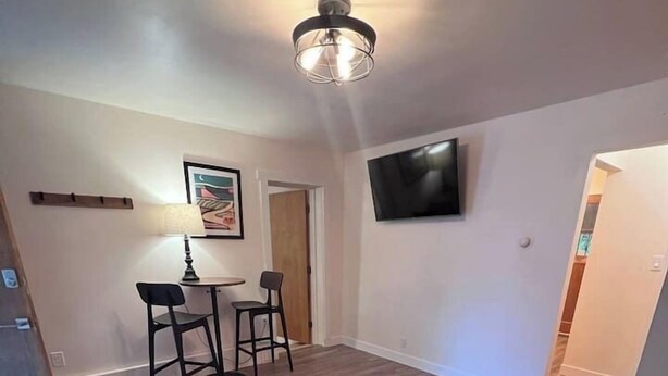 Una sala de estar con un sofá, una mesa de centro, un televisor instalado en la pared y un comedor con sillas y una mesa.