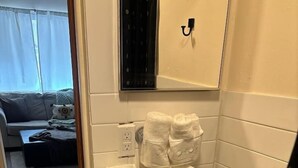 Un baño con inodoro, un cubo de basura negro y un perchero con varias toallas.