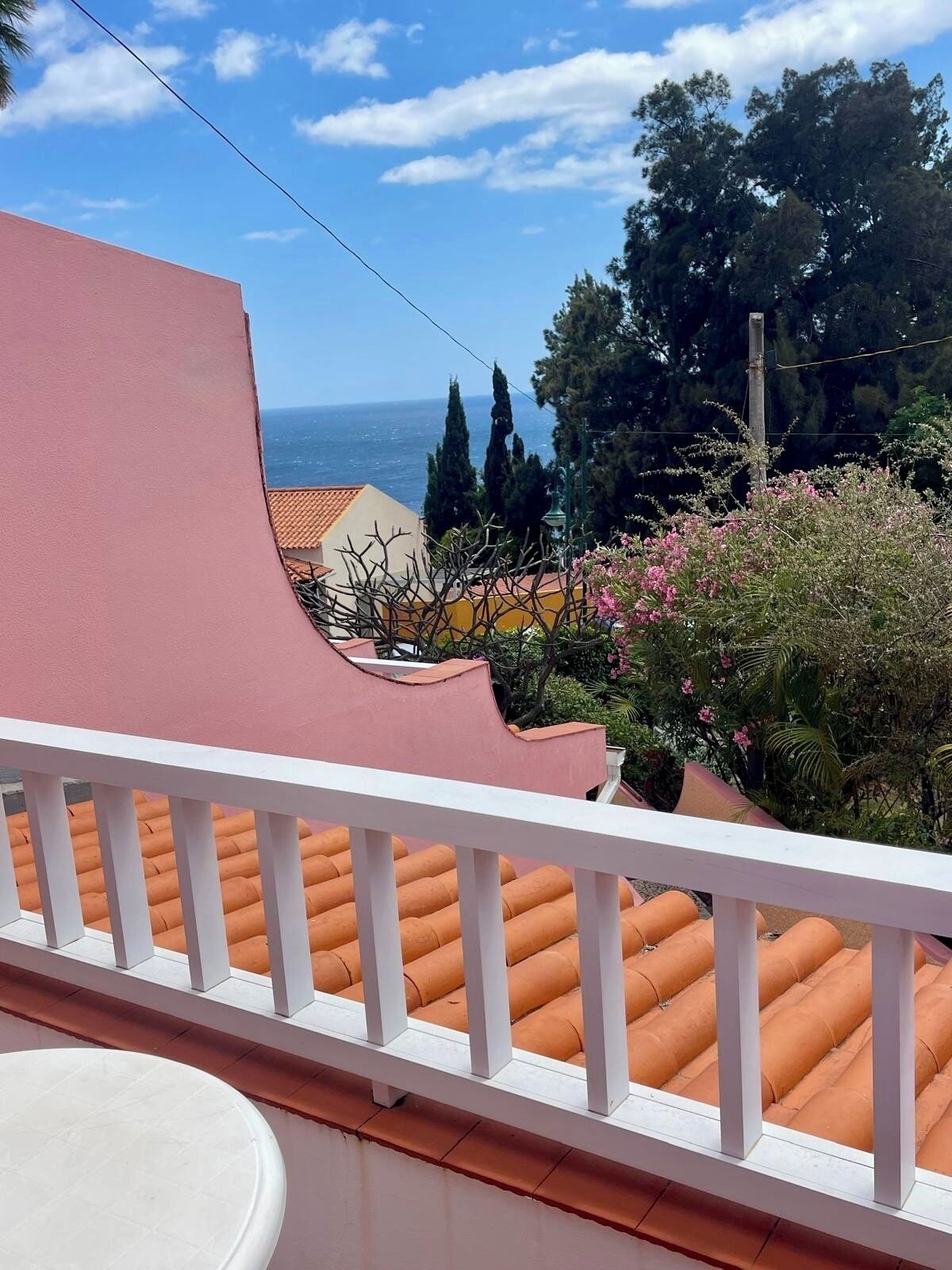 A balcony with orange tiles, a white railing, and a view of the sea and trees.