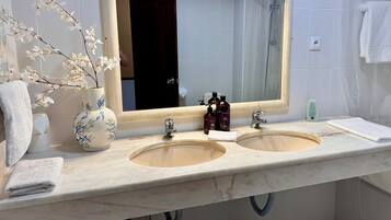 A bathroom with two sinks, a large mirror, a vase with flowers, and a towel rack.