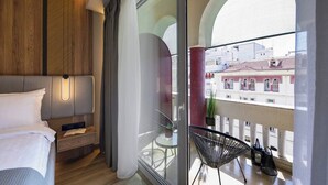 A modern hotel room with a bed, bedside table, and a balcony with a view of the city.